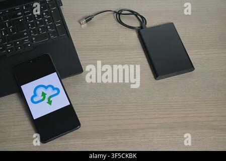 Workspace featuring a laptop, an external hard drive, and a phone with a cloud sync symbol. Stock Photo