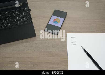 A workplace view showing a smartphone with a pie chart, a "Project" checklist, and a laptop. Stock Photo