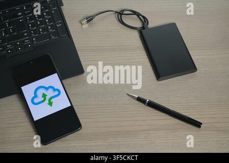 A desk layout with a laptop, external storage device, pen, and a smartphone showing cloud synchronization. Stock Photo