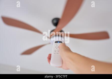 Hand using remote control to adjust ceiling fan speed in residential interior. Concept of home ventilation and everyday home comfort Stock Photo