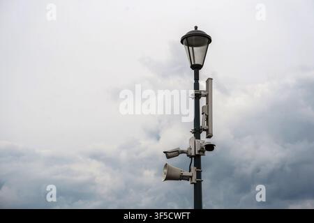 Grey street lamp pole equipped with multiple surveillance cameras and a loudspeaker, urban security infrastructure, public monitoring systems, smart city surveillance network, civic safety technology Stock Photo