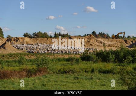 Wide angle shot of construction site excavation area with a central waste mound under a blue sky, an excavator working in the background, industrial terrain, building foundation development Stock Photo