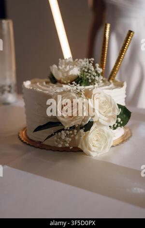 An elegant white wedding cake decorated with fresh cream roses and gold sparklers. Luxury marriage celebration, festive party dessert, sophisticated bridal banquet and romantic holiday event Stock Photo