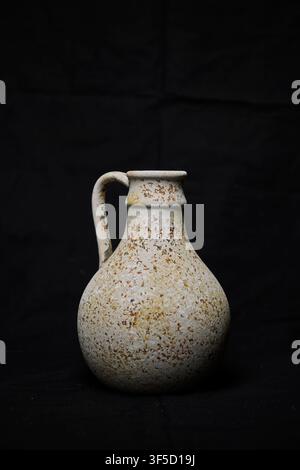Rustic stoneware jug standing with textured speckled surface on a plain black background Stock Photo