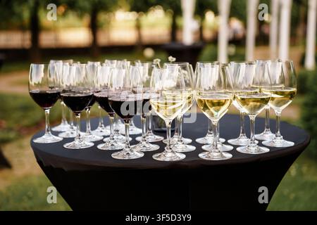 Many glasses of red and white wine arranged on a black covered table at an outdoor evening wedding reception or party event, catering hospitality, elegant garden banquet Stock Photo
