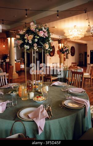 Elegant wedding banquet table with a tall gold centerpiece, pastel pink rose arrangements, sage green cloth, and warm lighting in a grand hall, romantic banquet reception Stock Photo