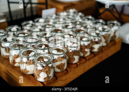 Rows of chocolate mousse and marshmallow desserts in small glass jars arranged on a wooden board for a catering buffet event and parties Stock Photo