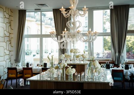 Elegant dining room featuring a large white chandelier and a centerpiece of white hydrangeas, ideal for wedding or luxury banquet event Stock Photo