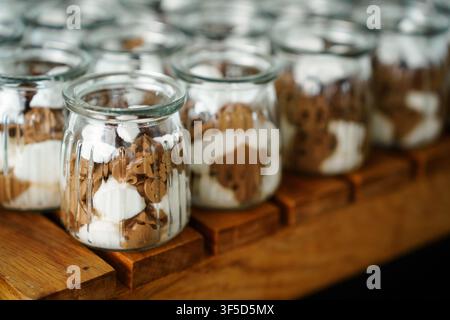 Layered chocolate and vanilla mousse cups in glass jars served on a rustic wooden board, perfect for catering, weddings, and sweet dessert tables, gourmet catering, sweet treats, party food Stock Photo