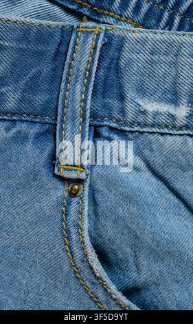 Faded blue denim fabric showing textile texture with yellow stitching and metal rivet detail Stock Photo
