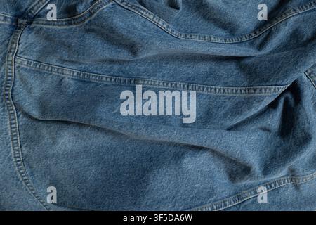 Blue crumpled denim fabric showing its texture and stitched seams Stock Photo