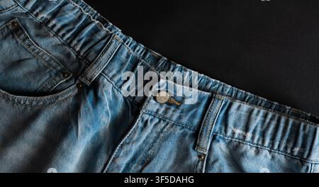 Close-up showing worn blue denim fabric with waistband, button, and pocket details on black Stock Photo