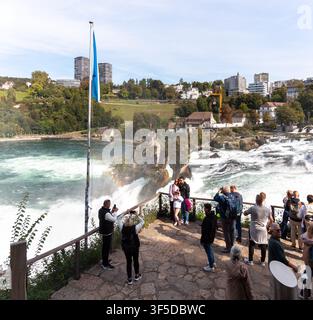 NEUHAUSEN, SWITZERLAND - SEPTEMBER 13, 2025: A diverse group of tourists taking photos and enjoying a powerful rushing waterfall from an observation p Stock Photo