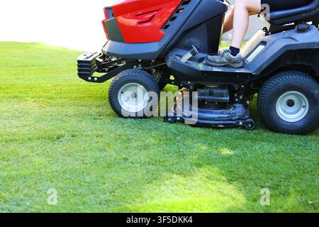 Ride-on lawn mower cutting fresh green grass in a landscaped park, showcasing professional lawn care and grounds maintenance. Stock Photo