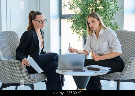 Two businesswomen discussing presentation on laptop during meeting in modern office Stock Photo