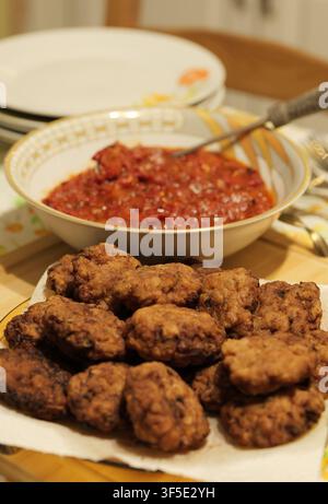 Plate of fried meatballs sitting on paper towel with a bowl of chunky red tomato sauce and empty plates in the background, signaling a homemade meal r Stock Photo