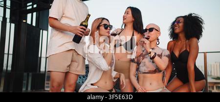 Diverse friends enjoying drinks at a rooftop party, celebrating summer lifestyle Stock Photo