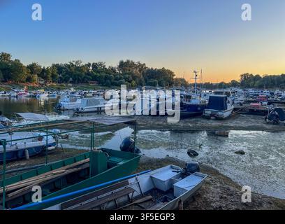 Exposed mud and dried riverbed visible under stranded boats during Danube River drought in Serbia. Stock Photo