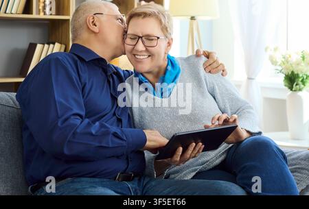 Happy senior couple using tablet at home, sharing affection and learning together Stock Photo