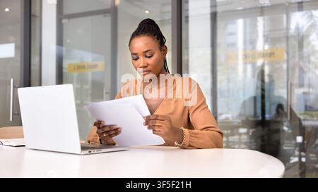 Focused African businesswoman reading documents at office desk Stock Photo