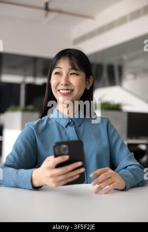 Smiling woman holding smartphone at office desk Stock Photo