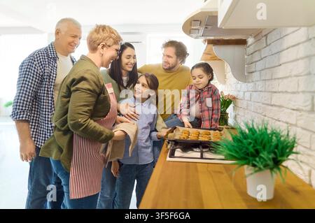 Smiling multigenerational family taking cookies from oven in bright kitchen Stock Photo