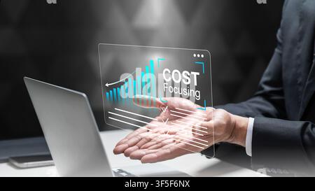 A businessman in a suit interacts with a digital holographic display showing a rising bar chart and COST Focusing text over a laptop, symbolizing fina Stock Photo
