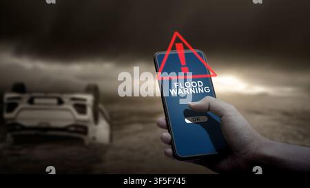A hand holds a smartphone showing a flood warning alert, with an overturned car partially submerged in water under a dark, stormy sky in the backgroun Stock Photo