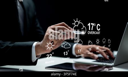 A professional in a suit interacts with a digital holographic weather forecast display showing temperatures and icons over a laptop and tablet on a de Stock Photo