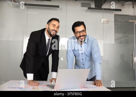 Businessmen leaning over desk with infographic papers and laptop Stock Photo