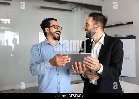 Multiethnic happy colleagues laughing, reviewing content on digital tablet Stock Photo