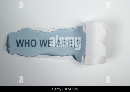 A creative concept image showing the phrase 'WHO WE ARE.?' revealed beneath a strip of torn white paper on a light blue background, representing ident Stock Photo