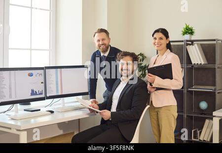 Smiling business team of three colleagues in modern office with analytics Stock Photo