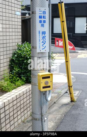 A yellow pedestrian push-button box for traffic signals mounted on a utility pole with Japanese signage along a sidewalk in Tokyo, Japan. Stock Photo