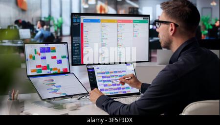Project Manager Reviews Agile Tasks On Digital Scrum Board During Meeting. Stock Photo