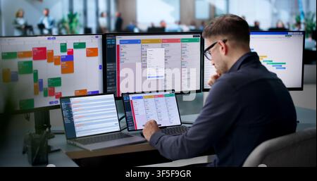 An Agile Project Manager Updates The Scrum Board Using Laptop And Tablet. Stock Photo