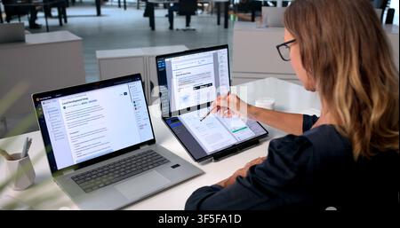 Mature Woman Uses Dual Computers To Organize Files And Improve Teamwork. Stock Photo