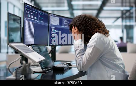 Tired African Software Engineer Rubs Head While Coding Late At Desk. Stock Photo