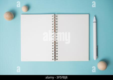 Workspace with empty notebook, pen and wooden ball on blue background. Flat lay, top view with copy space. Minimal office table desk concept. Stock Photo