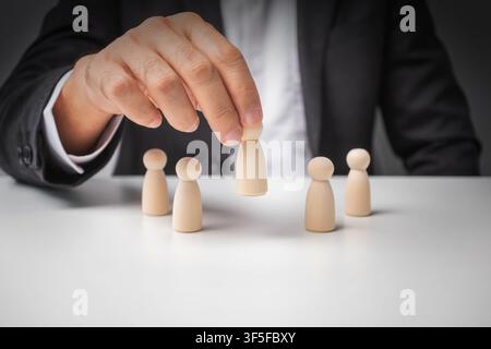 Businessman pick up leads from other wooden dolls on white desk. Successful business team leader. Leadership concept. Stock Photo