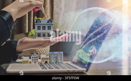 Global proptech and smart city innovation concept. Hands holding a model home with a futuristic cyber globe hologram and computer keyboard. Stock Photo
