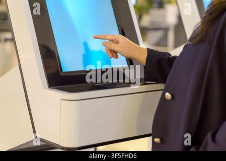Close-up of a person's hand interacting with a digital touch screen on a modern white self-service kiosk, likely for check-in or service in a public p Stock Photo
