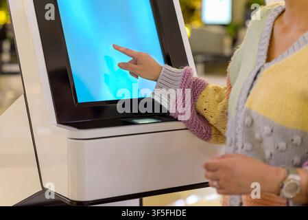 Close-up of a person's hand interacting with a digital touch screen on a modern white self-service kiosk, likely for check-in or service in a public p Stock Photo