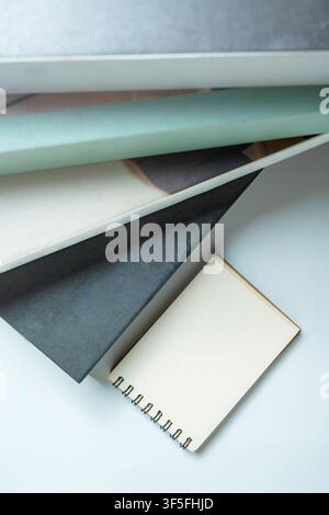 A stylish collection of various notebooks and a small spiral-bound notepad stacked diagonally on a clean, light-colored surface, ideal for office, pla Stock Photo