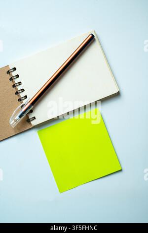 Top-down view of essential office supplies featuring a small spiral notebook, a pen, and a bright neon green adhesive sticky note on a textured gray b Stock Photo