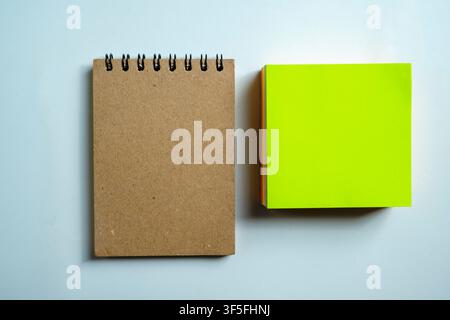 A top view of a blank brown spiral notebook and a stack of vibrant green sticky notes on a light blue desktop. Perfect for office, education, and plan Stock Photo