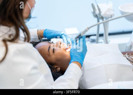Dentist in blue gloves and mask performing an oral hygiene procedure on a female patient Stock Photo