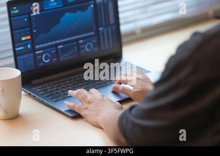 Hands working on a laptop displaying financial data, with coffee on desk. Concept of online trading, data analysis, remote work, and modern digital bu Stock Photo
