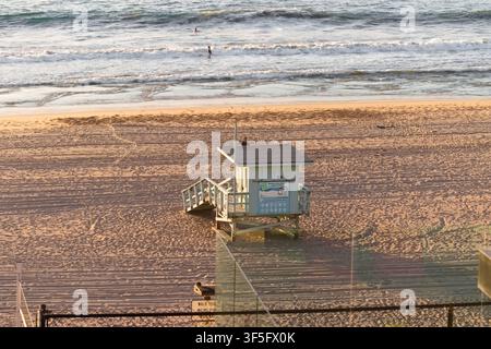 Lifeguard tower on sandy beach at sunset with gentle waves rolling in behind it. Stock Photo