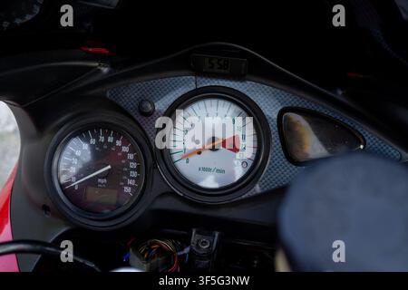 Motorbike dashboard with speedometer and tachometer. Red needle on tachometer shows engine RPM. Digital display reads current speed. Black textured pa Stock Photo